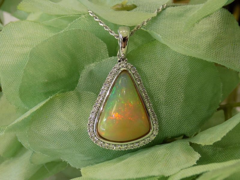 Opal pendant necklace with a diamond halo on a green background.