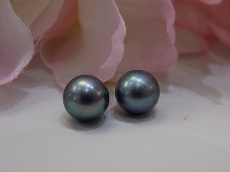 Two dark gray Tahitian pearls with green iridescence on a white surface