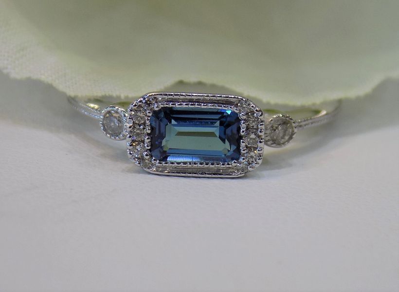 Silver ring with a rectangular blue gem and surrounding halo of small diamonds.