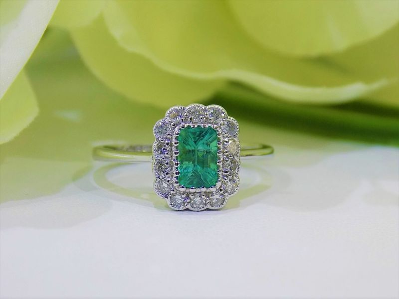 Emerald and diamond ring, rectangular green gemstone, surrounded by diamonds, on a white surface