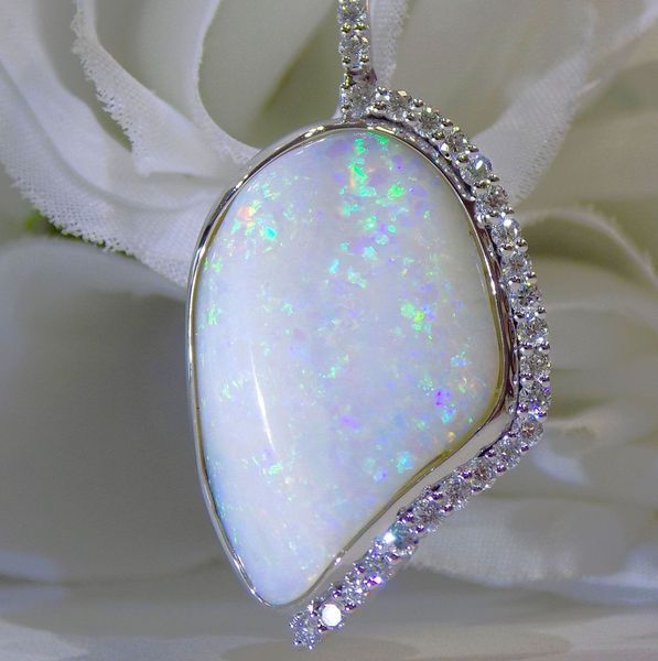 White opal pendant with diamond accents, set against a blurred white flower.