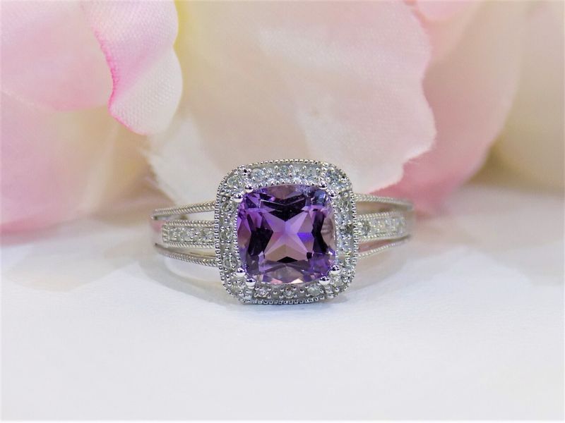 Amethyst and diamond ring on a white surface with blurred pink flower background