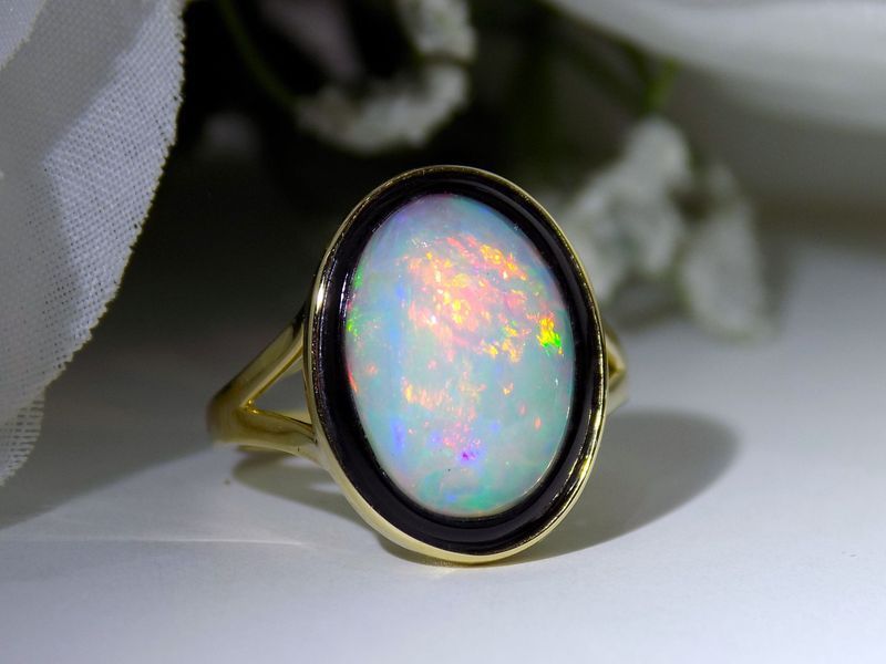 Gold ring with an oval opal gemstone surrounded by a black enamel borde