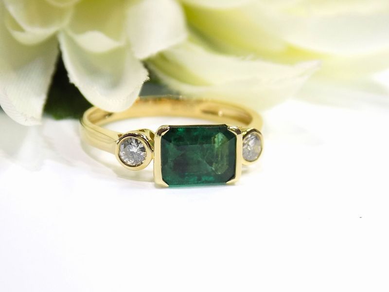 Gold ring with a rectangular emerald center stone and two round diamond side stones
