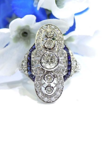 Diamond and sapphire art deco ring on a white surface, in front of blue and white flowers