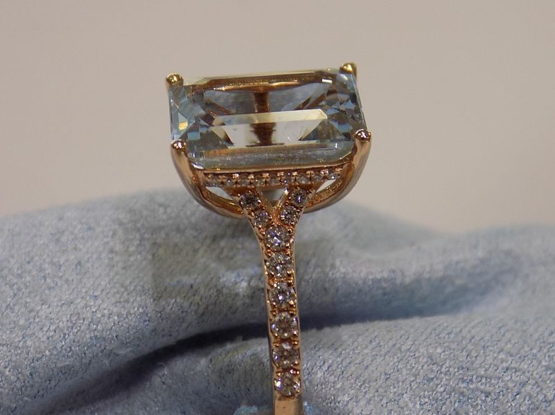 Ring with a large, light blue rectangular gemstone in a gold setting with small accent stones