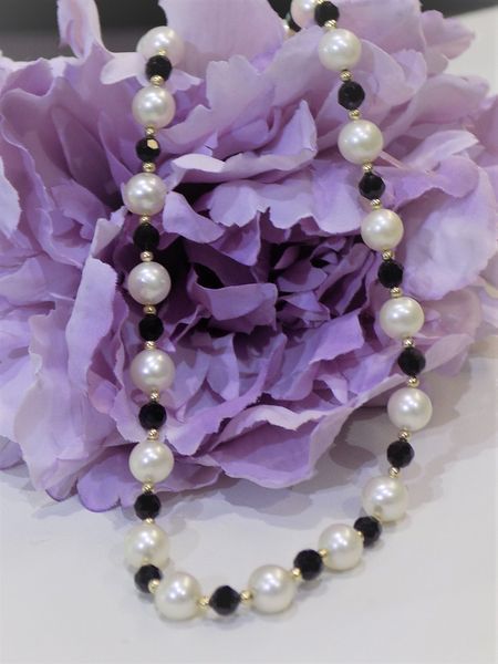 Pearl necklace with black accent beads against purple flower