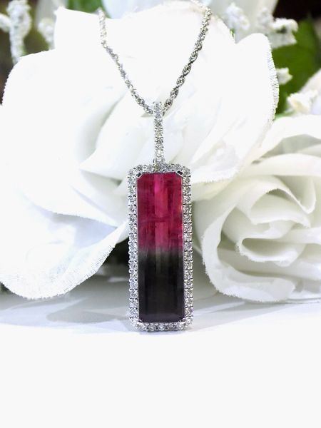 Necklace with a rectangular pink and black gemstone, surrounded by diamonds, on a white rose background.
