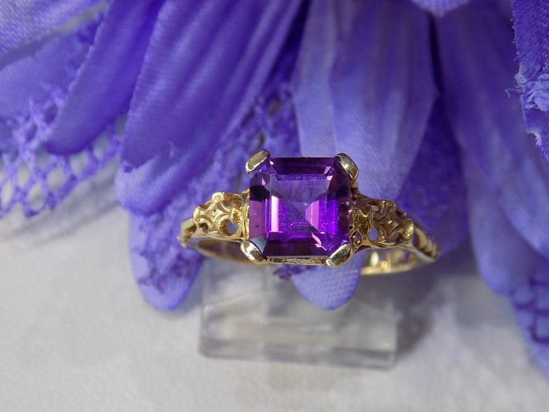 Gold ring with a large, purple gemstone set against purple flowers