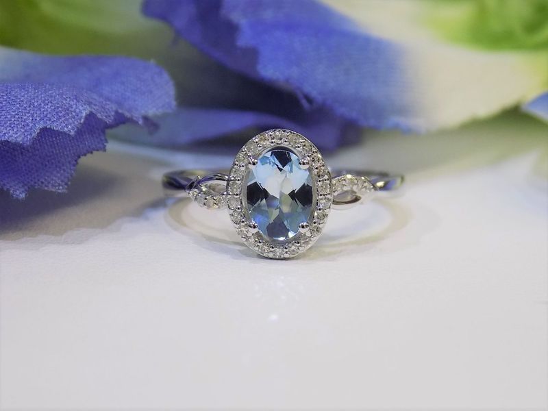 Oval aquamarine and diamond halo ring on white surface