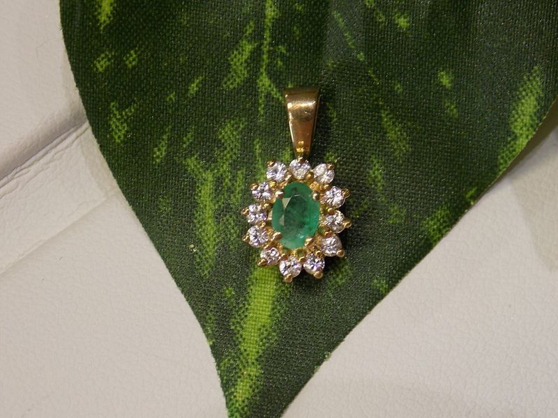 Gold pendant with teardrop emerald and diamond halo on green leaf