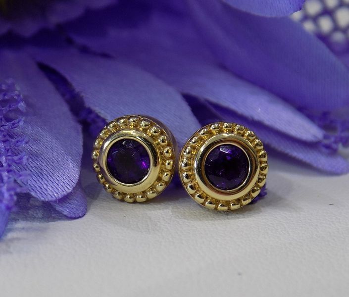 Gold stud earrings with purple gemstones, placed on a purple flower