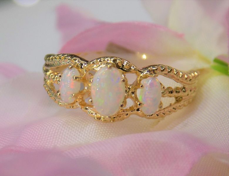 Gold ring with three oval opals on a pink background