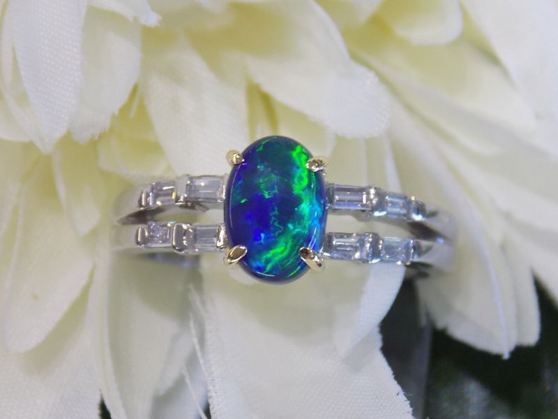 Black opal ring with green and blue flashes, set in gold prongs