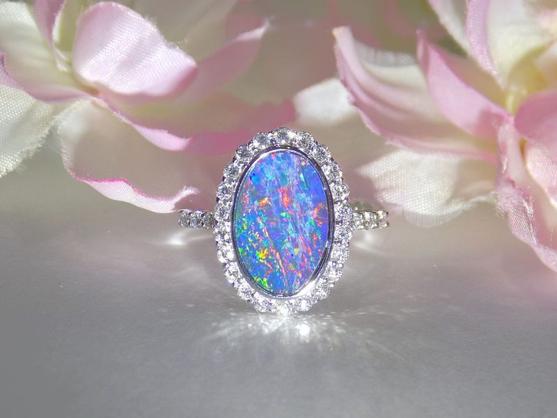 Oval opal ring with diamond halo set against pink flowers