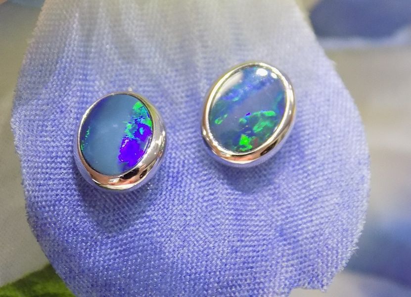 Oval opal stud earrings with silver settings, displaying blue and green fire