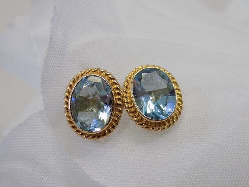 Gold earrings with oval, light-blue gemstones, set against a white