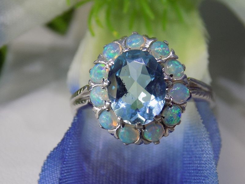 Oval blue gemstone ring with small opal halo on a blue fabric