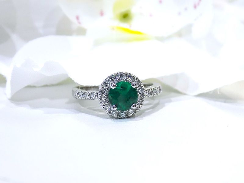 Emerald and diamond halo ring on a white surface