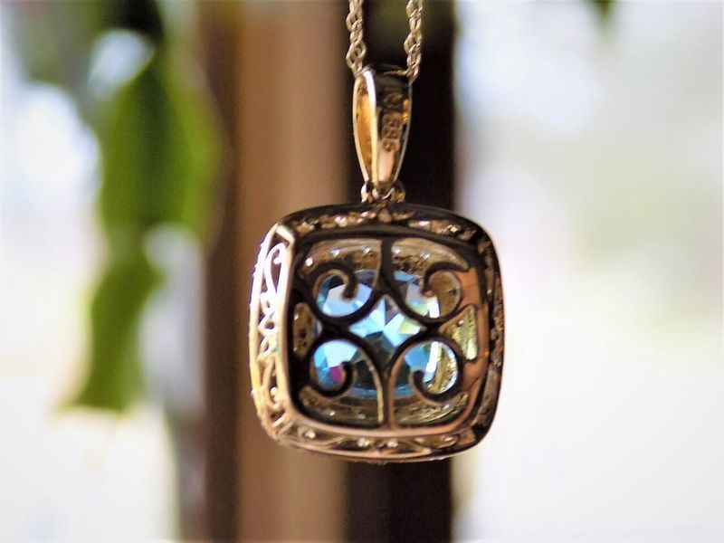 Gold filigree pendant with a blue, iridescent gem, hanging on a gold chain