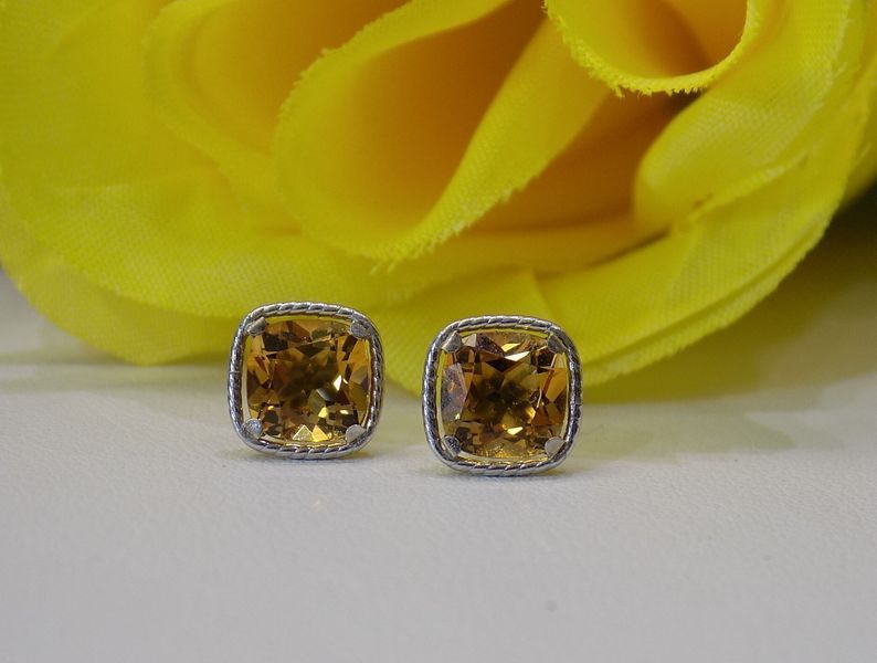 Gold stud earrings with square, yellow-orange gemstones, set on a white surface