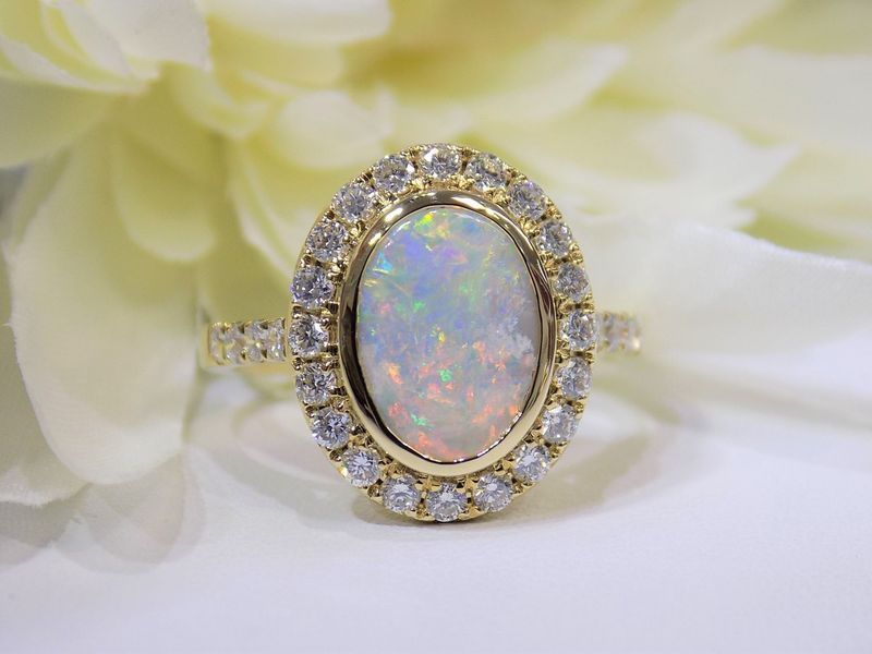Gold ring with a large opal surrounded by diamonds, resting on a white surface