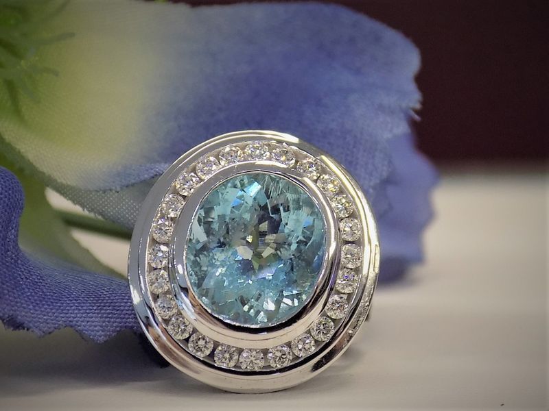Oval aquamarine gemstone ring with diamond halo, set against blue fabric