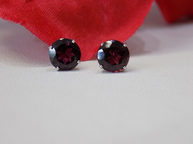 Garnet stud earrings on white surface with red fabric background