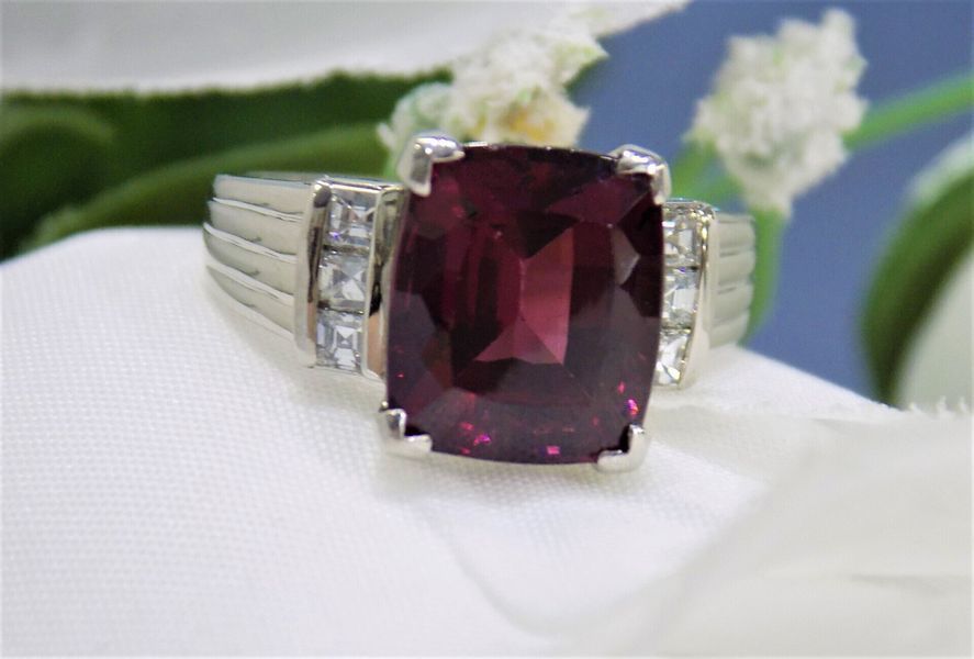 A white gold ring with a large, square-cut, dark red gemstone and smaller side stones