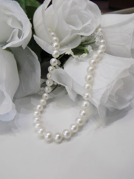 White pearl necklace draped over white roses
