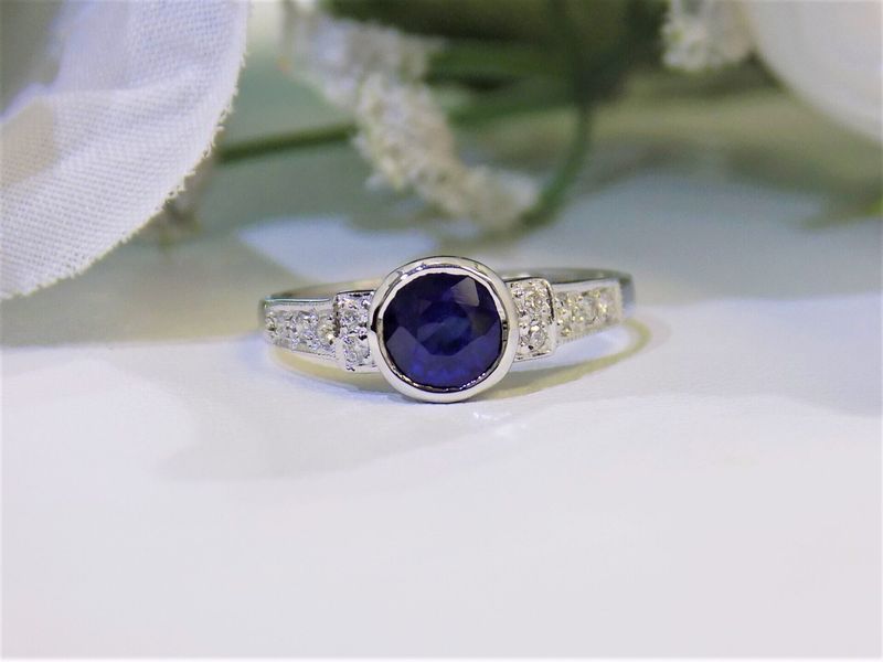 Sapphire and diamond ring on a white surface, with white flowers in the background