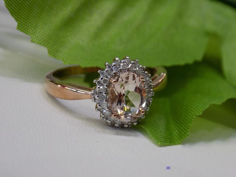 Rose gold ring with a peach-colored oval gemstone surrounded by white stones