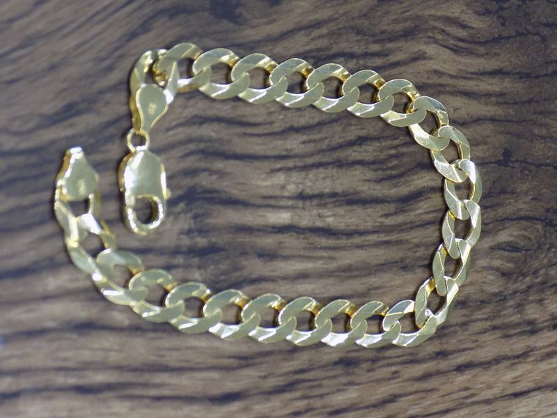 Gold curb chain bracelet on a dark wood surface