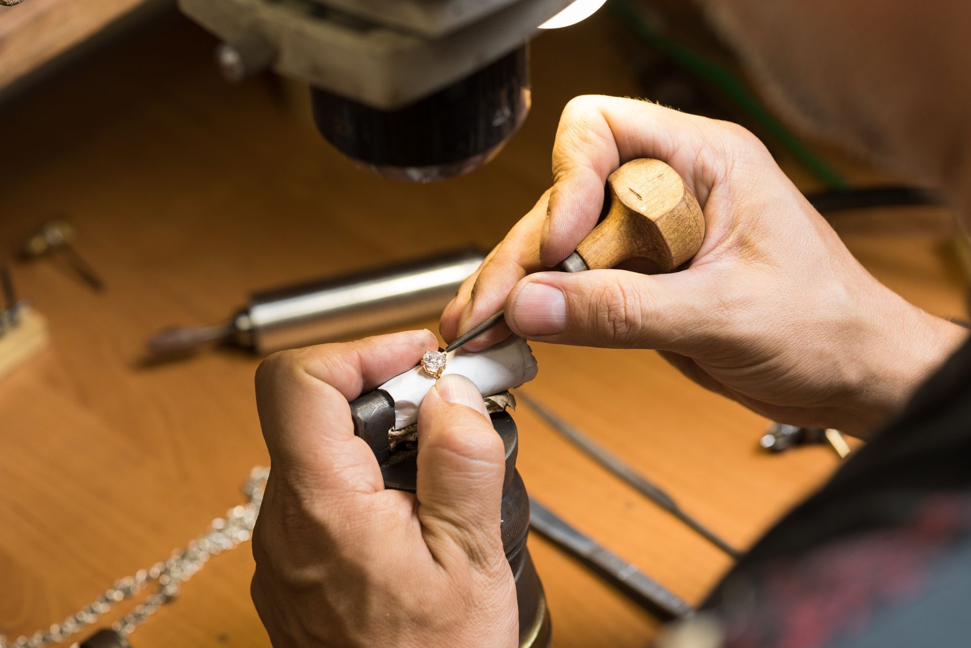 Jeweler using hand tools to work on a piece of jewelry under bright light