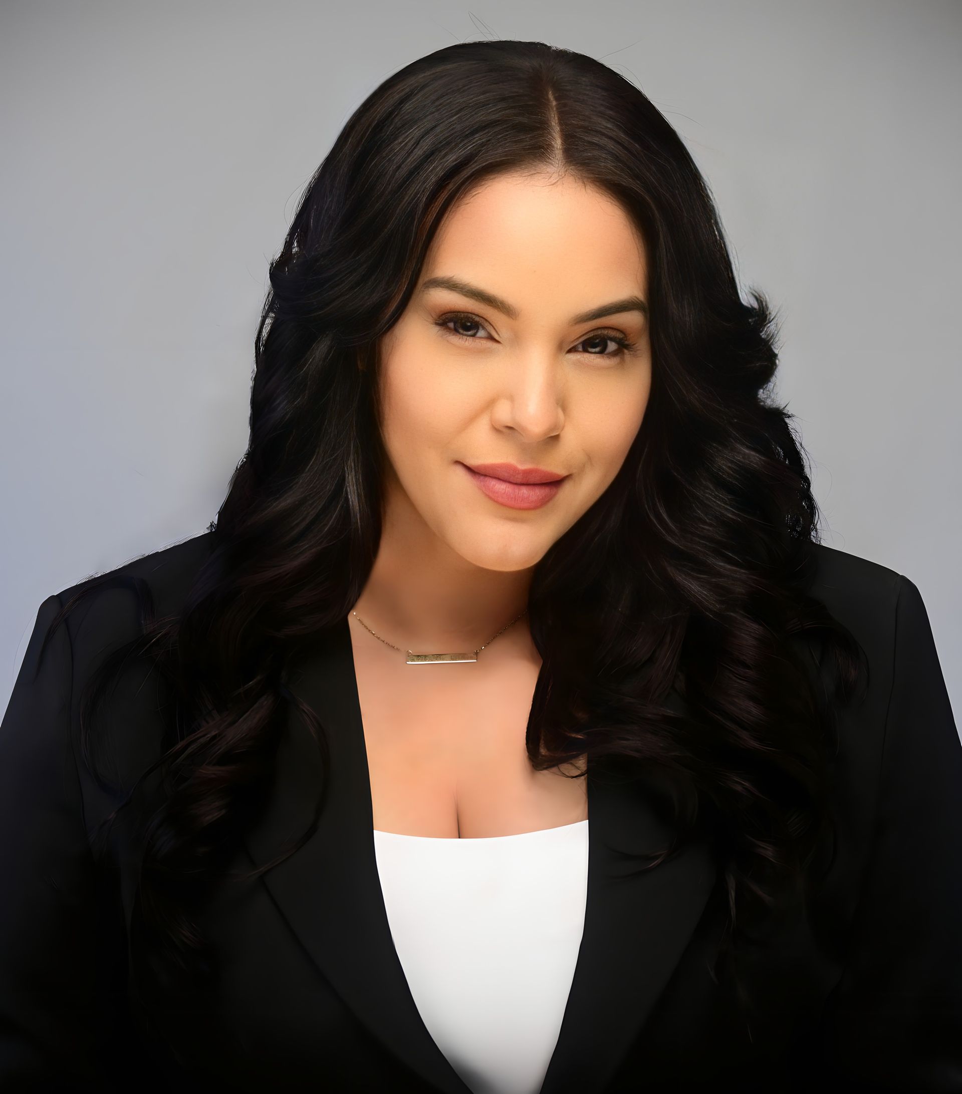 Woman in a black blazer and white top, with dark wavy hair, smiling at the camera.