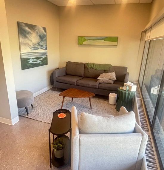 A cozy office with warm lighting, seascape paintings, and two couches facing each other. 