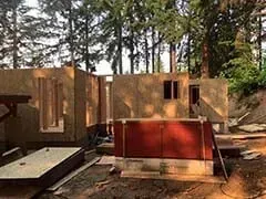 Partially built wooden structure with red panels in a wooded area