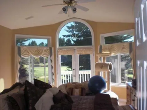 Bright living room with arched windows, white curtains, and dark couches; a blue exercise ball sits near the center.