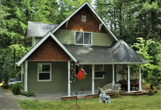 Small gray cabin with a porch in a wooded setting, with an orange hanging chair and lawn furniture.