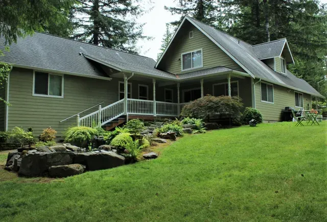 Large gray house with white trim, front porch, and landscaped lawn on a green hillside