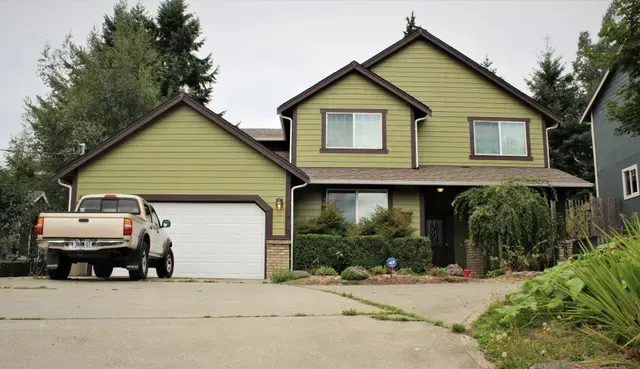 Suburban house with a white pickup truck parked in the driveway, front yard and trees visible.
