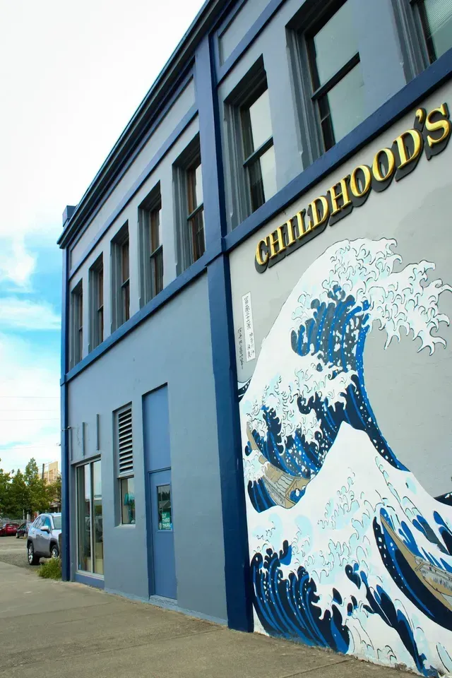 Blue building with a large wave mural and yellow sign reading “WHIDBEY HOODS”