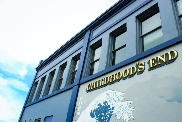 Blue building facade with gold “Childhood’s End” sign against a bright sky