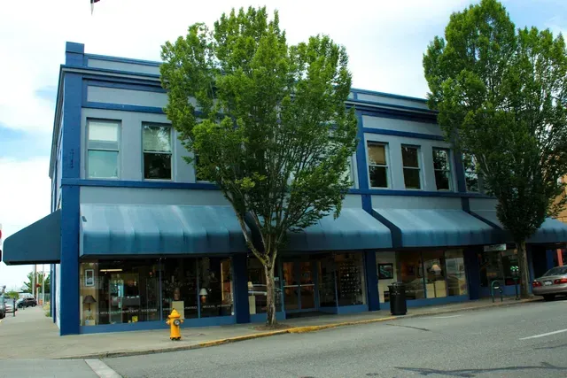 Blue two-story storefront building with awnings and trees on a street corner