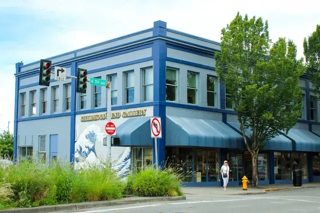 Blue two-story corner storefront with awnings, street signs, trees, and a pedestrian on the sidewalk