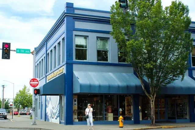 Blue corner building with awnings at a street intersection, with a tree, fire hydrant, and a pedestrian nearby