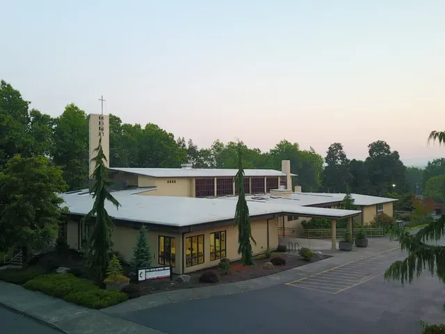 Modern low-rise building with a white roof, surrounded by trees and a paved driveway at dusk