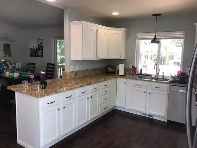 Bright kitchen with white cabinets, granite countertops, and a dining area by a window.