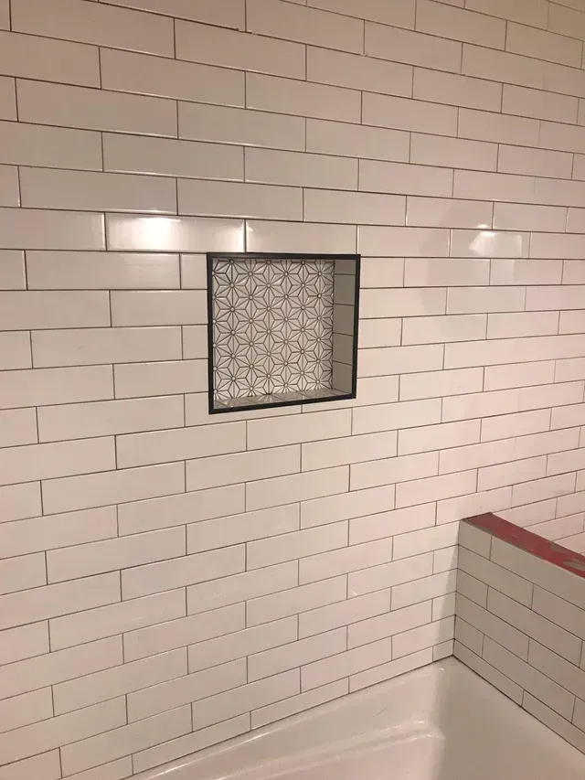 White tiled shower wall with a square frosted-glass window and tub edge with red trim