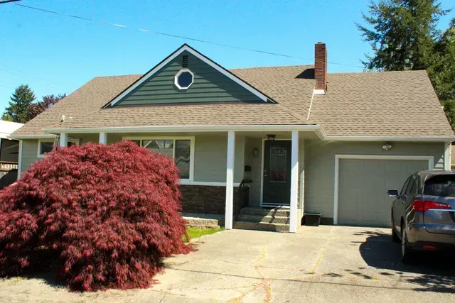Suburban house with a front porch, red shrub, and car parked in the driveway